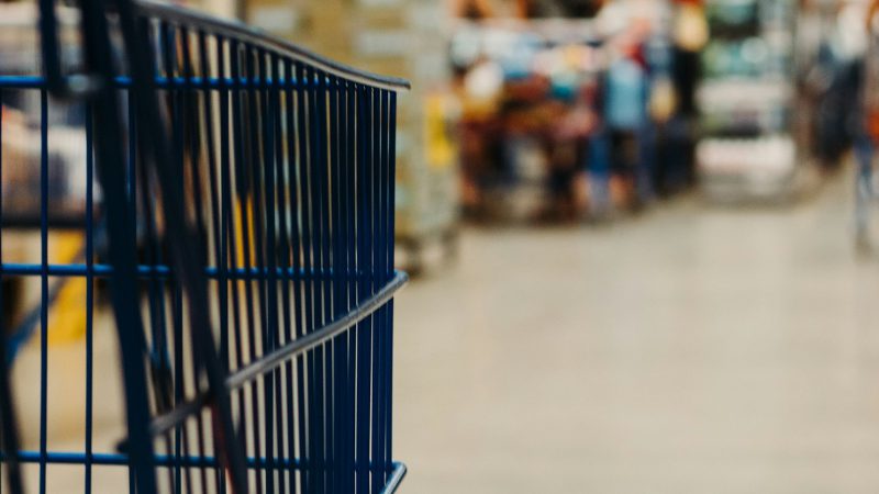 A blue metal shopping cart in a blurred grocery store aisle
