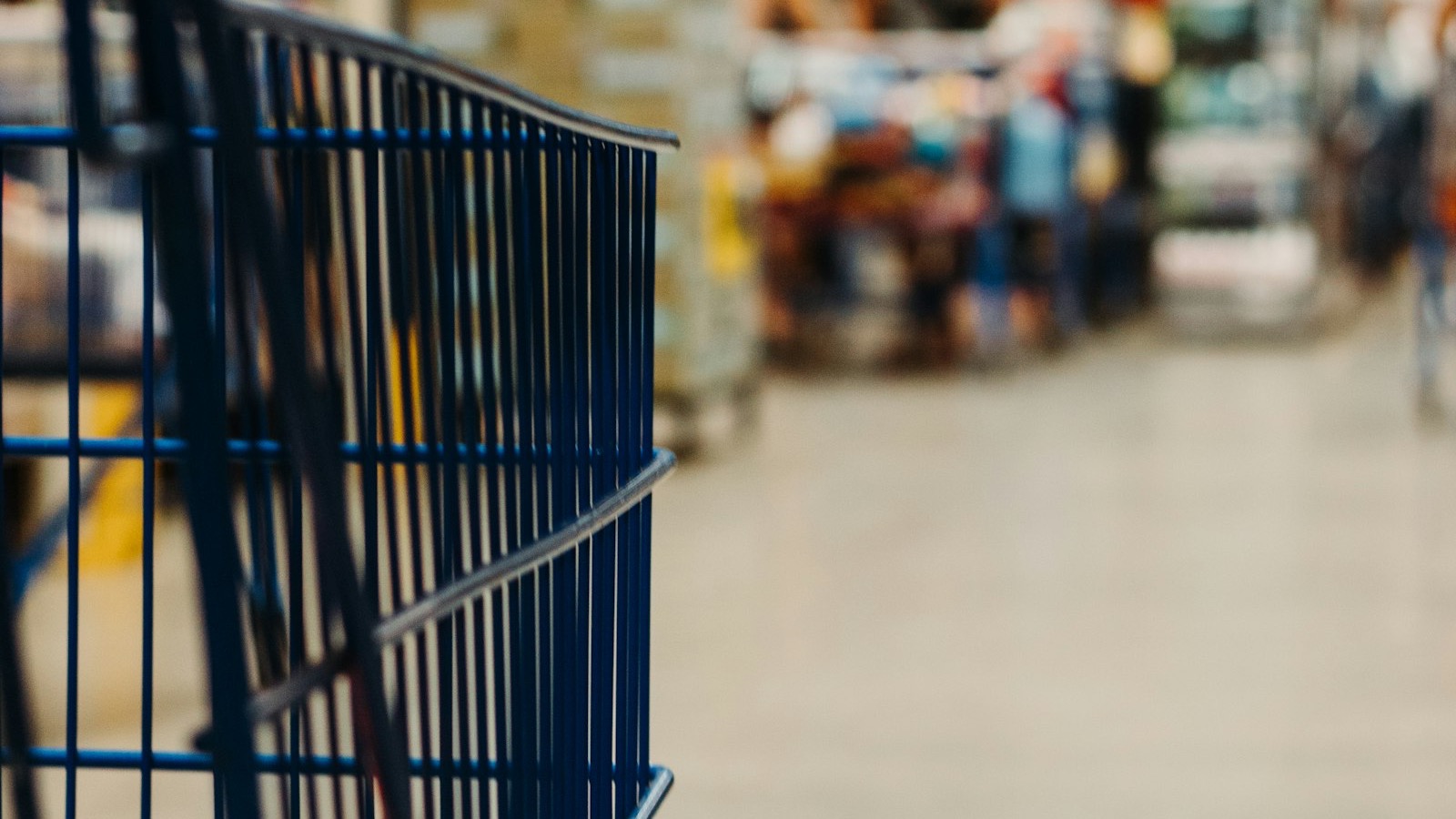 A blue metal shopping cart in a blurred grocery store aisle