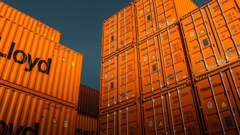 Stacked orange shipping containers against a deep blue sky