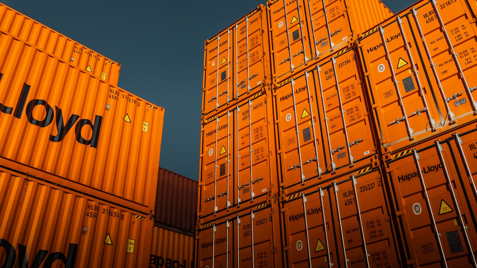 Stacked orange shipping containers against a deep blue sky